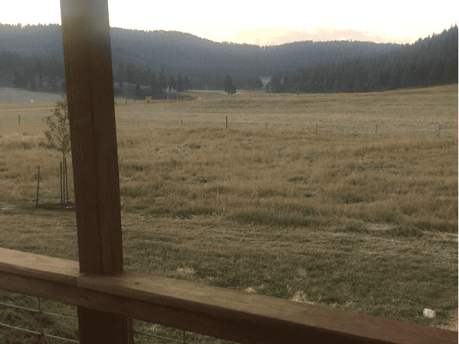 Views of a meadow and mountains in the distances from a cabin porch, something you can see on a road trip from Denver to South Dakota