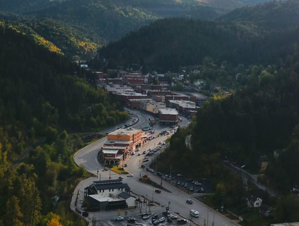 An aerial view of Deadwood, South Dakota. There are mountains with trees and in the middle of the valley is the town.